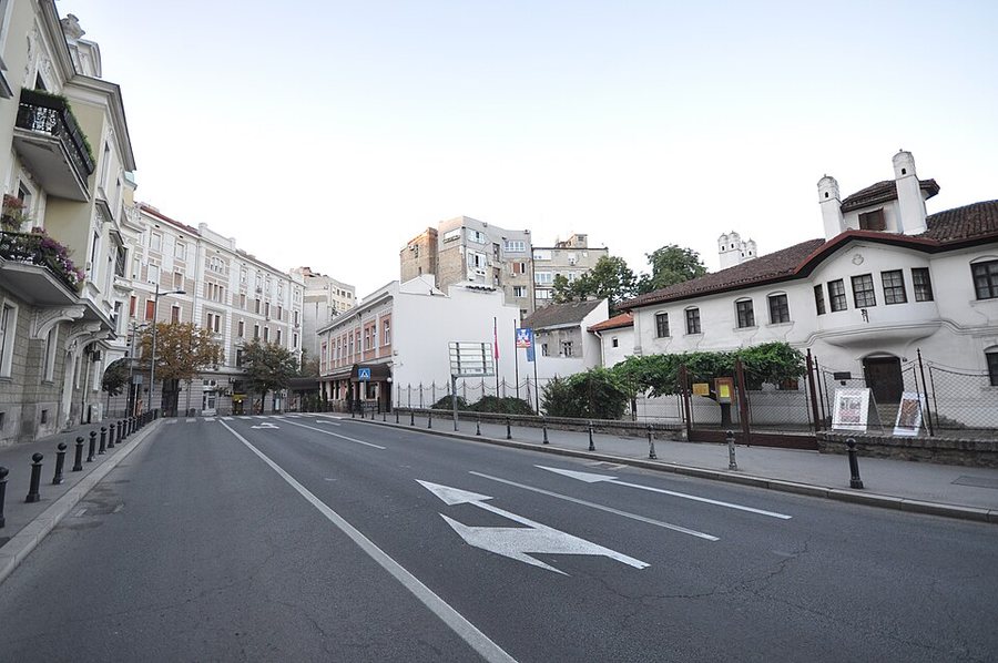 Pogled sa ulice na Konak kneginje Ljubice u Beogradu: bela dvospratna kuća sa crepnim krovom, belim dimnjacima i ogradom obraslom lozom, pored savremene ulice.
